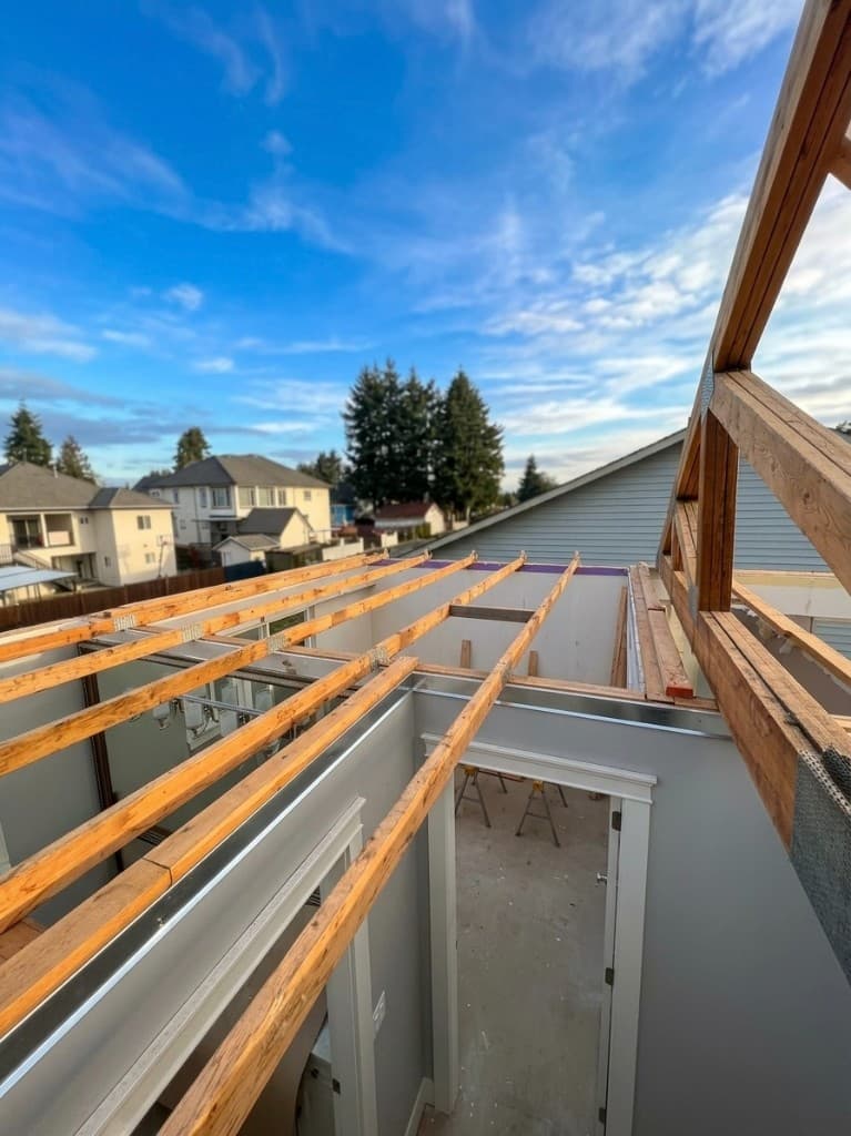 Structural wood framing and roof trusses inside a residential build under a clear blue sky